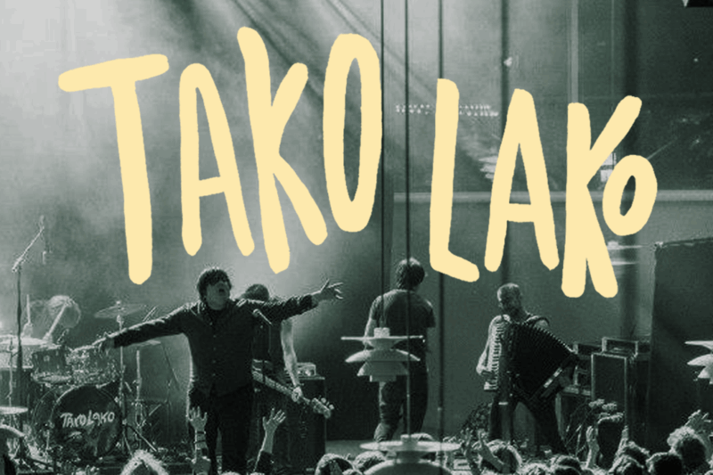 Tako Lako på scenen under en koncert med fuld energi og publikum i bevægelse. Bandets navn står skrevet med store gule bogstaver hen over billedet.
